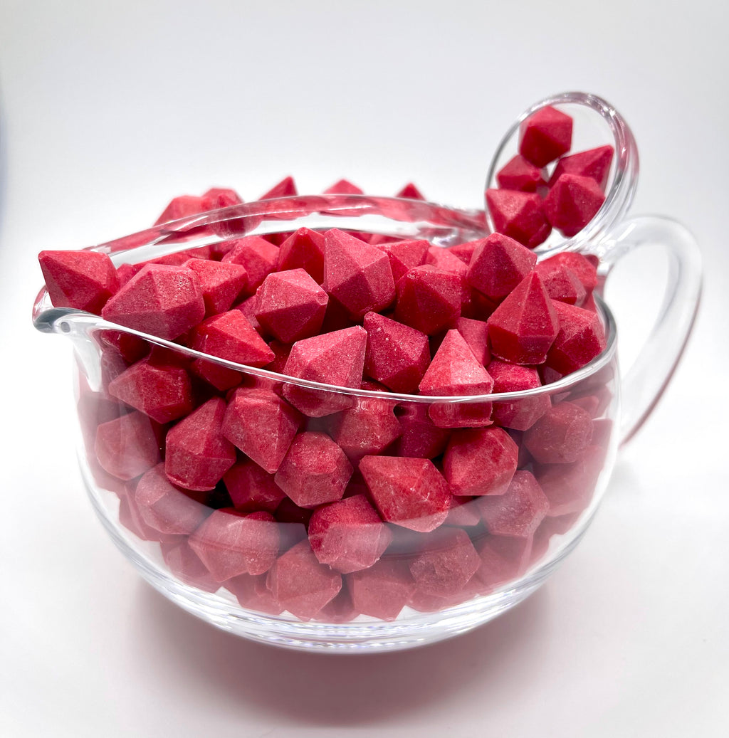 A clear bowl filled with red aphrodisiac candies, with a lid and on a white background.
